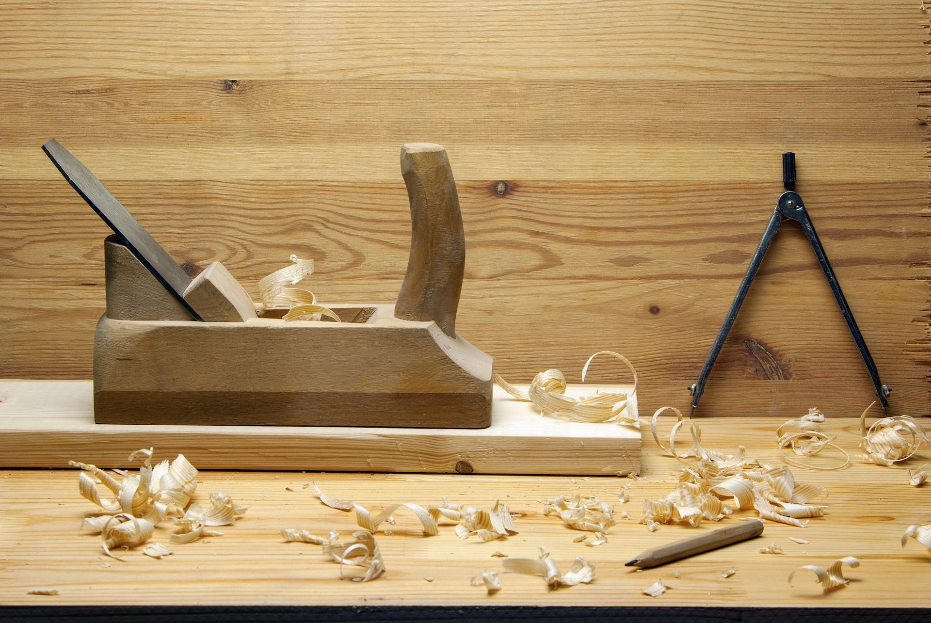 Hobelwaren Die Hobelwaren von HolzPartner in Rathenow stehen für höchste Präzision und Qualität – perfekt für Bauprojekte in Berlin und Brandenburg. Mit sorgfältig gehobelten Oberflächen bieten sie die ideale Grundlage für langlebige und ansprechende Holzarbeiten. Bildbeschreibung: Holzhandhobel auf einem Brett, umgeben von frischen Hobelspänen, daneben ein Bleistift und ein Metallzirkel auf einer Werkbank.