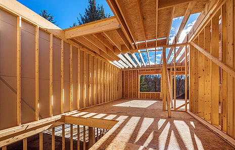 Das Konstruktions- und Bauholz von HolzPartner in Rathenow eignet sich ideal für den modernen Holzbau in Berlin und Brandenburg – ob für Hausbau, Dachkonstruktionen oder tragende Elemente. Stabil, nachhaltig und flexibel einsetzbar.  Bildbeschreibung: Holzrahmenbau eines Hauses im Bau, sichtbare Balkenkonstruktionen und Sonnenlicht, das durch die offenen Dachbalken fällt.