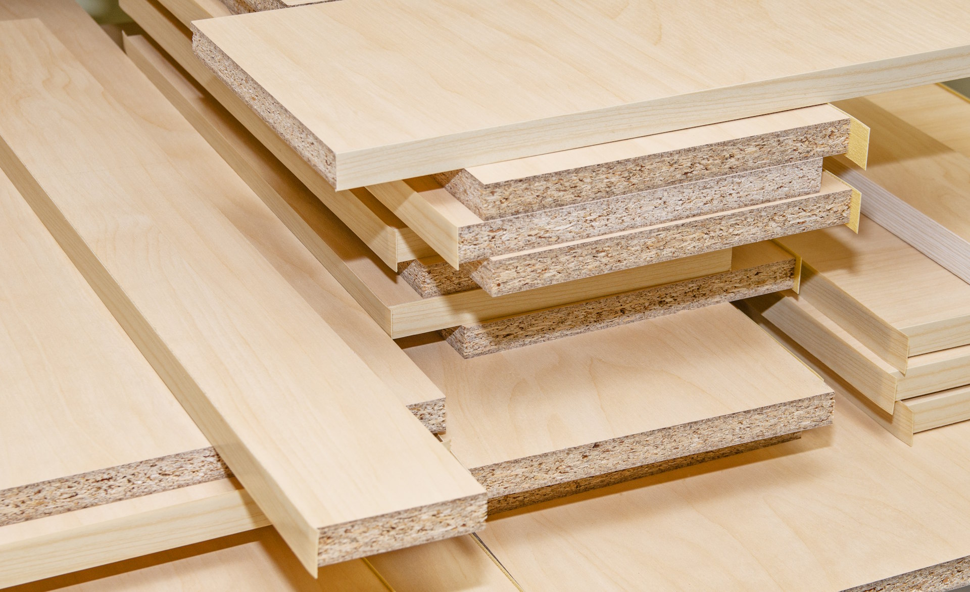 Plattenwerkstoff Die Plattenwerkstoffe von HolzPartner in Rathenow sind ideal für Möbelbau, Innenausbau und handwerkliche Projekte in Berlin und Brandenburg. Sie überzeugen durch hohe Stabilität, präzise Verarbeitung und eine pflegeleichte Oberfläche. Bildbeschreibung: Mehrere helle Spanplatten mit furnierter Oberfläche, gestapelt und zugeschnitten, mit deutlich sichtbarer Schichtstruktur an den Kanten.
