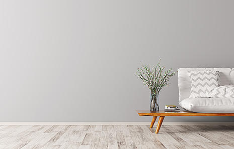 Linoleumboden von HolzPartner in Rathenow – die nachhaltige und stilvolle Bodenlösung für Ihr Zuhause in Berlin und Brandenburg. Linoleum überzeugt durch Natürlichkeit, Robustheit und ein zeitloses Design – ideal für Wohn- und Arbeitsbereiche.  Bildbeschreibung: Minimalistisch eingerichtetes Wohnzimmer mit hellem Linoleumboden, grauer Wand, Sofa und Dekoration.