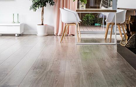 Vinylboden Vinylboden von HolzPartner in Rathenow bietet eine elegante Lösung für stilvolles Wohnen in Berlin und Brandenburg. Er überzeugt durch seine moderne Holzoptik, hohe Strapazierfähigkeit und pflegeleichte Oberfläche – ideal für stark genutzte Wohnbereiche. Bildbeschreibung: Helles Wohnzimmer mit großen Glasfronten, weißen Möbeln und grauem Vinylboden in Holzoptik, der den Raum modern und freundlich wirken lässt.
