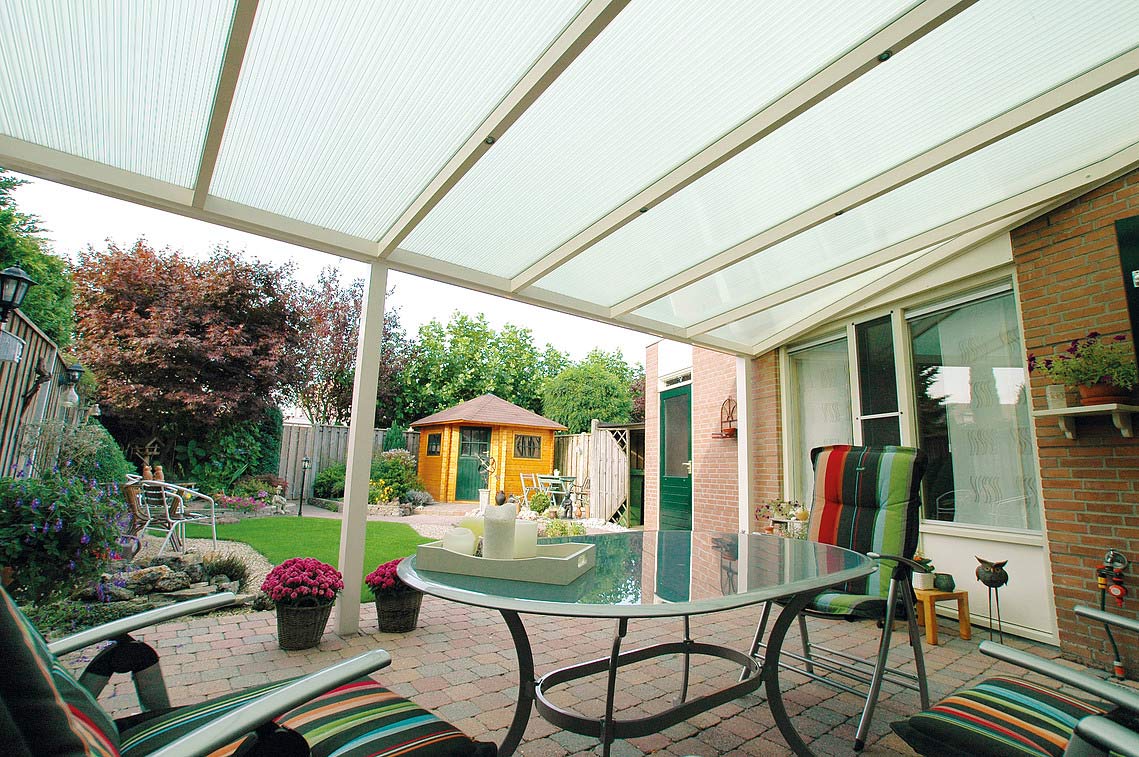 Terrassenüberdachung mit Stegplatten HolzPartner in Rathenow bietet langlebige Terrassenüberdachungen mit Stegplatten für Berlin und Brandenburg – stabil, wetterbeständig und lichtdurchlässig. So schaffen Sie einen geschützten Außenbereich, der Komfort und Helligkeit optimal verbindet. Bildbeschreibung: Überdachte Terrasse mit transparenten Stegplatten, Gartenmöbeln und Blick auf einen gepflegten Garten mit Holzgartenhaus.