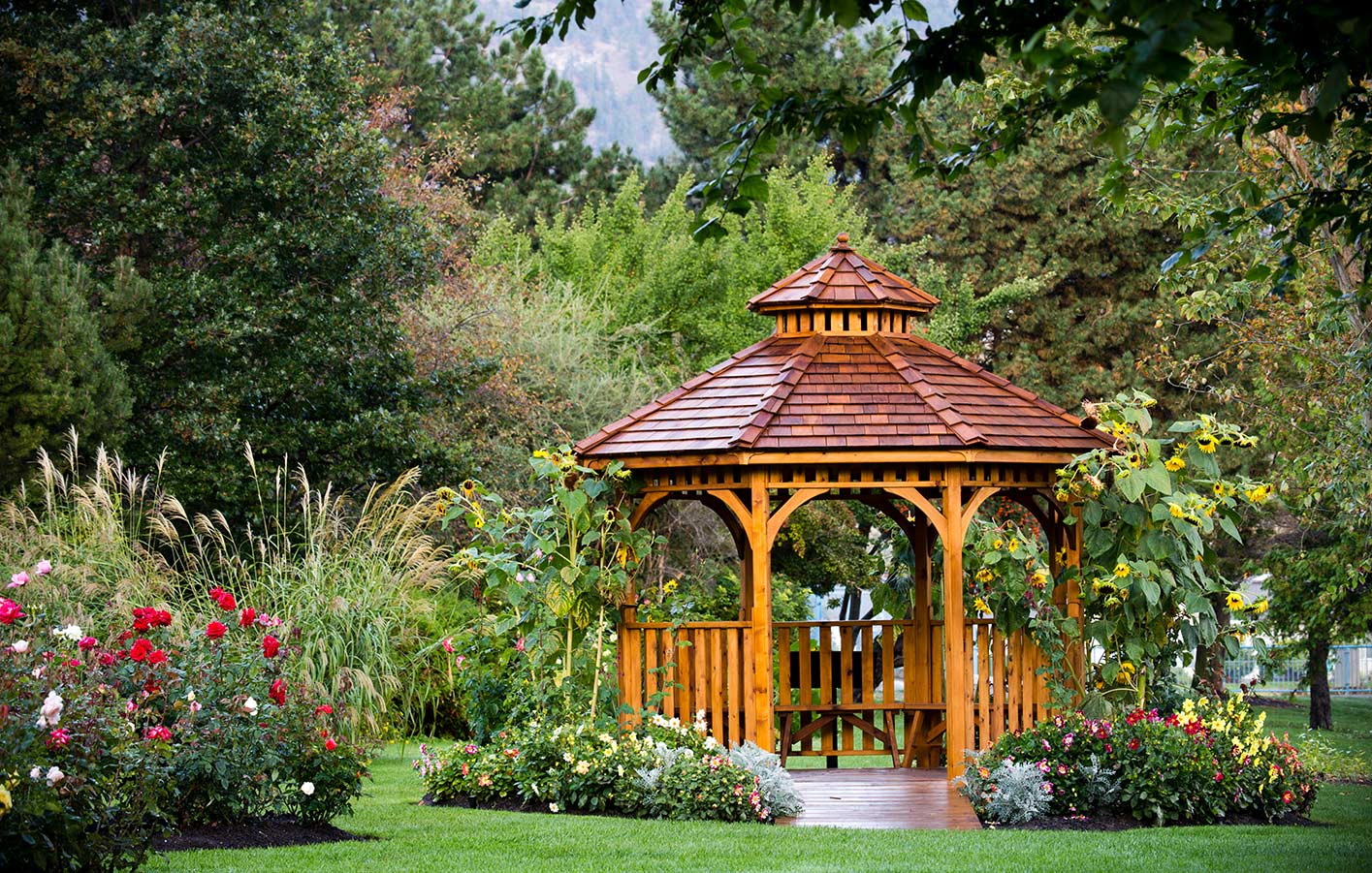 HolzPartner in Rathenow bietet stilvolle Gartenpavillons aus Holz für Berlin und Brandenburg – perfekt als eleganter Rückzugsort, für gemütliche Stunden oder als Highlight in Ihrem Garten. Langlebig, wetterbeständig und individuell gestaltbar.  Bildbeschreibung: Holzpavillon mit geschwungenem Dach, umgeben von bunten Blumenbeeten und grüner Gartenlandschaft.