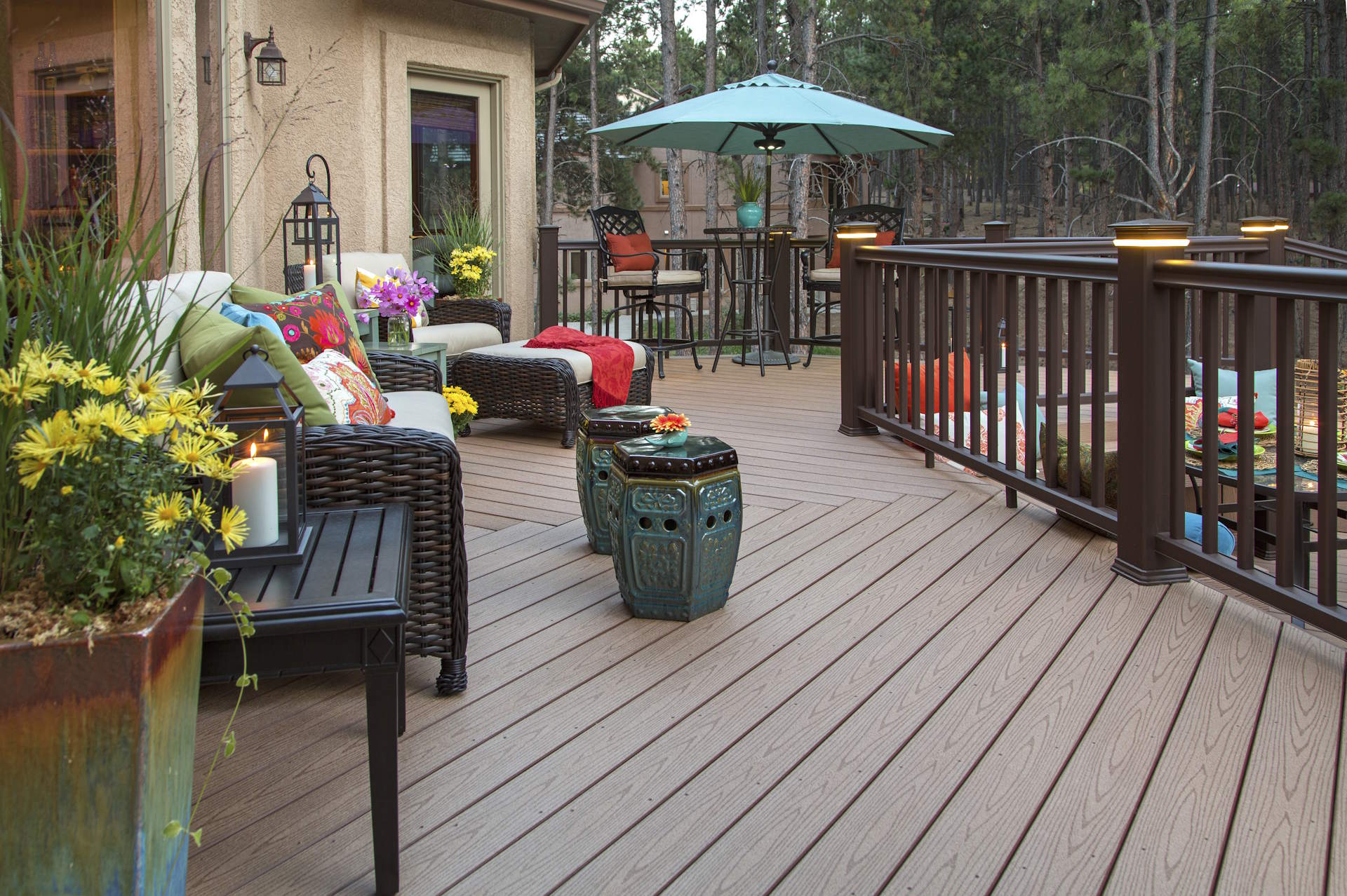 Terrassendielen aus WPC HolzPartner in Rathenow bietet hochwertige Terrassendielen aus WPC für Berlin und Brandenburg – pflegeleicht, wetterfest und besonders langlebig. Gestalten Sie Ihre Terrasse modern und komfortabel mit einer pflegearmen Alternative zu Holz. Bildbeschreibung: Gemütlich eingerichtete Terrasse mit braunen WPC-Dielen, Gartenmöbeln, bunten Kissen, Laternen, Pflanzen und einem Sonnenschirm.