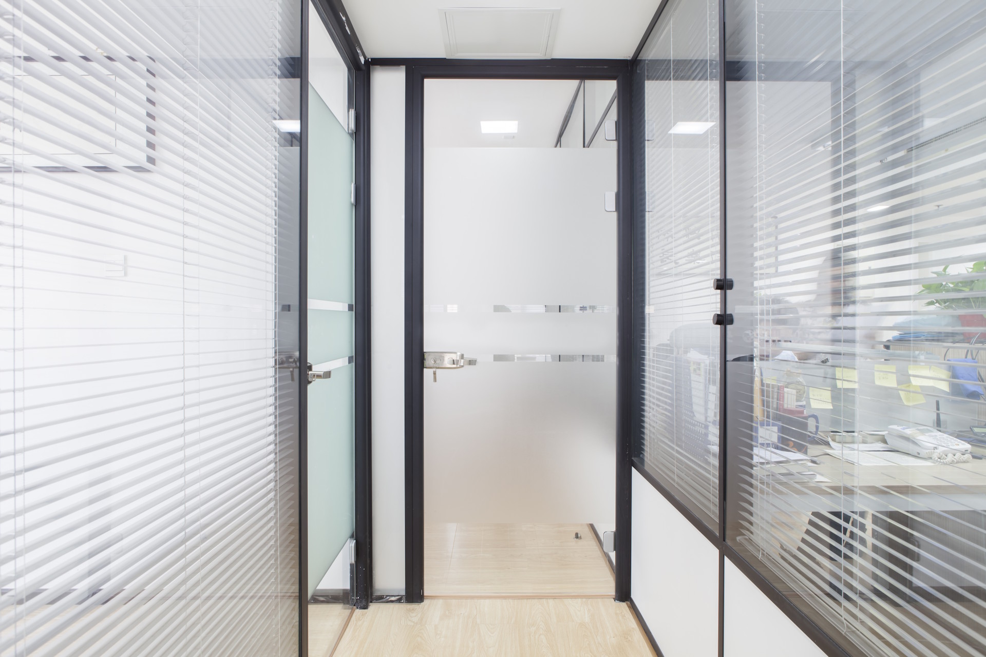 Glastüren Die Glastüren von HolzPartner in Rathenow sind die ideale Wahl für moderne Wohn- und Arbeitsbereiche in Berlin und Brandenburg. Sie sorgen für lichtdurchflutete Räume, schaffen ein offenes Ambiente und kombinieren Eleganz mit Funktionalität. Bildbeschreibung: Glastür mit Milchglas-Einsatz und Edelstahlbeschlägen in einem modernen Büroflur mit Glaswänden und Jalousien.