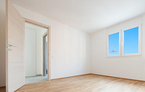 Innentüren Innentüren von HolzPartner in Rathenow sind die ideale Wahl für stilvolle und langlebige Raumgestaltung in Berlin und Brandenburg. Sie verbinden modernes Design mit hoher Funktionalität und fügen sich harmonisch in jede Wohnumgebung ein. Bildbeschreibung: Helle Innentür aus Holz in einem modernen, leeren Raum mit Parkettboden, weißen Wänden und zwei Fenstern mit blauem Himmel.