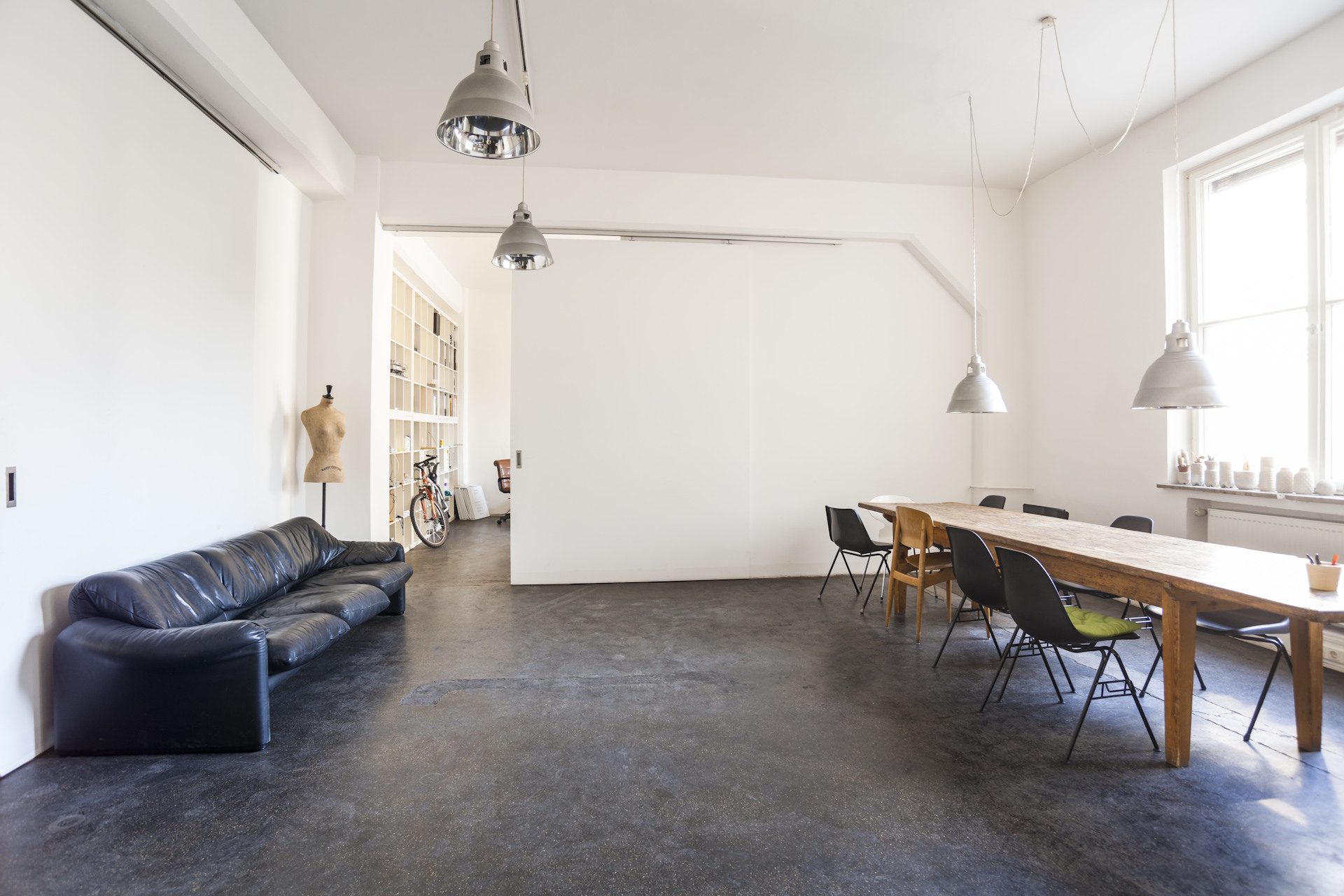 Raumteiler Die Raumteiler von HolzPartner in Rathenow sind die perfekte Lösung für flexible Raumgestaltung in Berlin und Brandenburg. Sie ermöglichen es, offene Bereiche bei Bedarf zu trennen, ohne auf ein modernes, helles Wohngefühl zu verzichten. Bildbeschreibung: Schlichter, weißer Raumteiler in einem Loft mit schwarzem Ledersofa, großem Holztisch und minimalistischer Einrichtung.