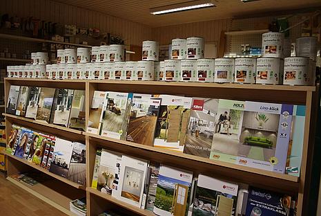 Holzschutz Die Lösungen und Konzepte für Holzschutz von HolzPartner in Rathenow verbinden hochwertige Lasuren, Öle und Farben mit individuellen Anwendungsideen für innen und außen. So wird Ihr Holz optimal vor Umwelteinflüssen geschützt und gleichzeitig ästhetisch aufgewertet – ideal für Bauprojekte in Berlin und Brandenburg. Bildbeschreibung: Präsentationsregal mit verschiedenen Holzschutz-Produkten und Katalogen zu Bodenbelägen, Türen und Gestaltungskonzepten.