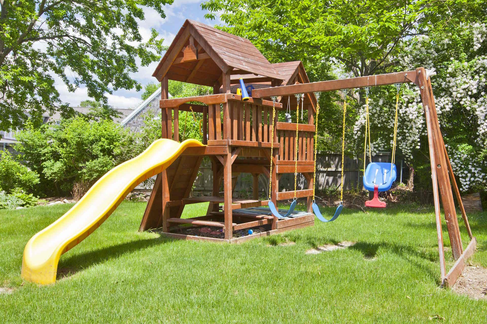 Kinderspielgeräte für den Garten Mit den Kinderspielgeräten von HolzPartner in Rathenow gestalten Familien in Berlin und Brandenburg ihren Garten zu einem sicheren Spielparadies. Robuste Holz-Spielgeräte mit Schaukeln, Rutschen und Klettertürmen bieten Kindern Bewegung, Abenteuer und Freude im eigenen Zuhause. Bildbeschreibung: Holzspielgerät im Garten mit gelber Rutsche, Kletterturm und Schaukeln auf einer grünen Rasenfläche, umgeben von Bäumen und Sträuchern.