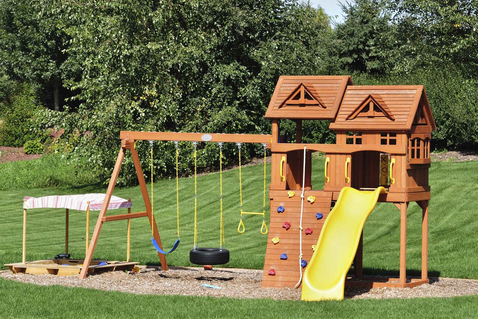 Kinderspielgeräte für den Garten Mit den Kinderspielgeräten von HolzPartner in Rathenow verwandeln Sie Ihren Garten in Berlin und Brandenburg in einen abwechslungsreichen Abenteuerspielplatz. Hochwertige Holzgeräte mit Schaukeln, Rutsche, Kletterwand und Sandkasten bieten Kindern Spielspaß und Sicherheit im eigenen Zuhause. Bildbeschreibung: Kinderspielgerät aus Holz mit gelber Rutsche, Kletterwand, Doppelturm, Schaukeln und Sandkasten auf einer gepflegten Rasenfläche.